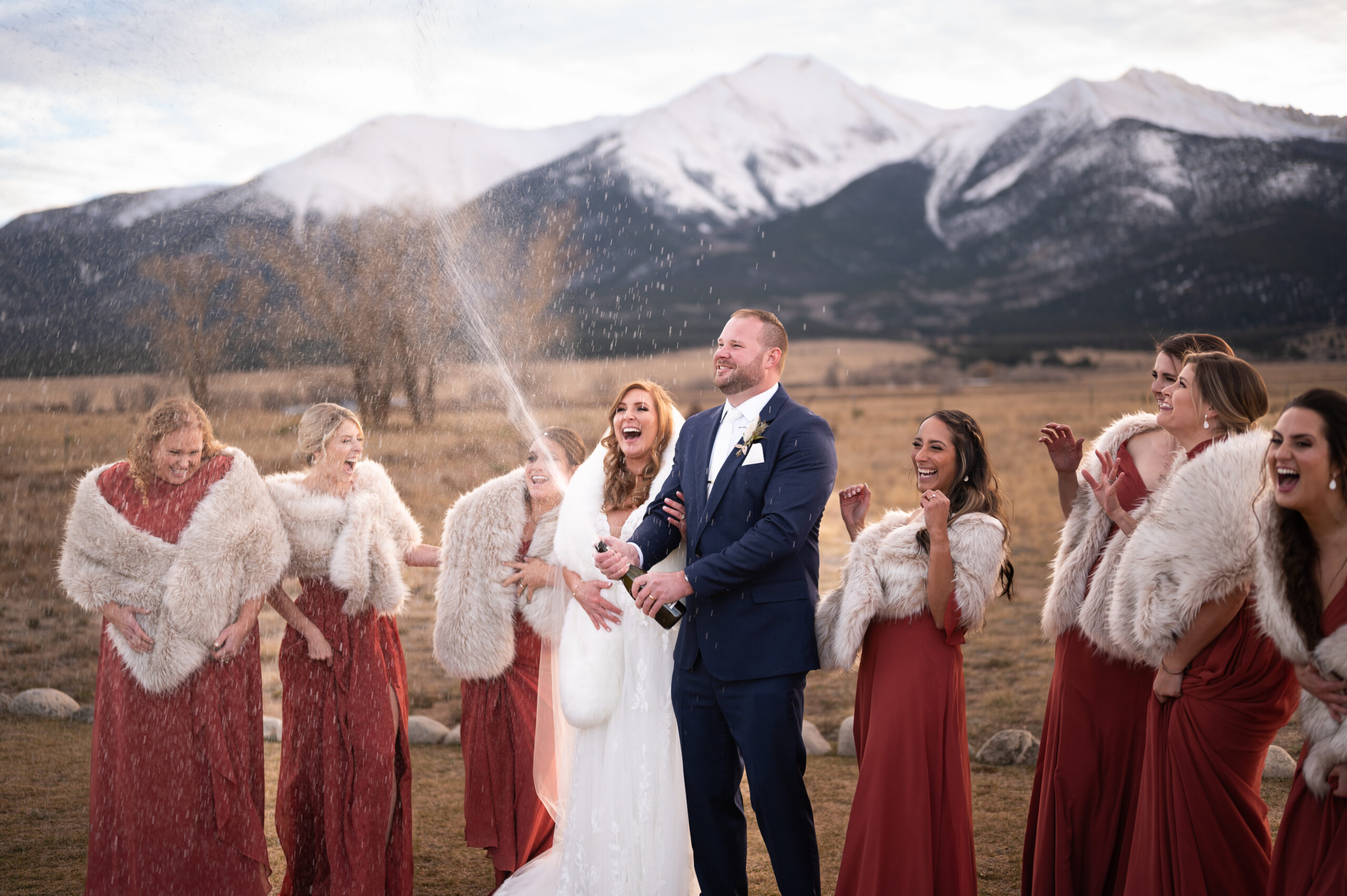 birde & groom spraying champagne all over wedding party in front of a beautiful mountain range in Colorado, Mount Princeton at The Barn at Sunset Ranch.